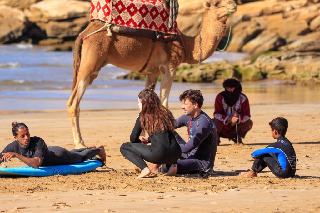 A group of beginners taking surf lessons in Tamraght, Morocco, learning to ride the waves at Paddle Out Morocco Surfhouse.