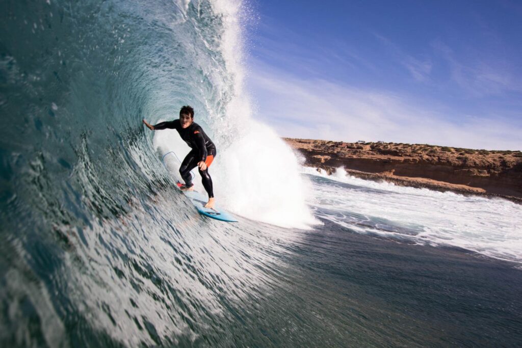 Surfer riding waves at Taghazout Beach, a top spot for adventure tourism in Agadir